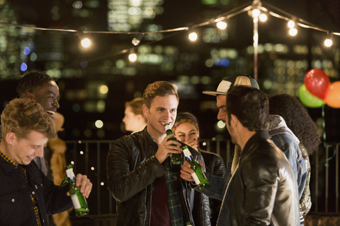 Junge Männer trinken Bier auf einer Dachterrassenparty, lizenzfreies Stockfoto