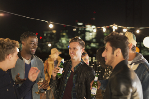Junge Männer trinken Bier und unterhalten sich auf einer Dachterrassenparty, lizenzfreies Stockfoto