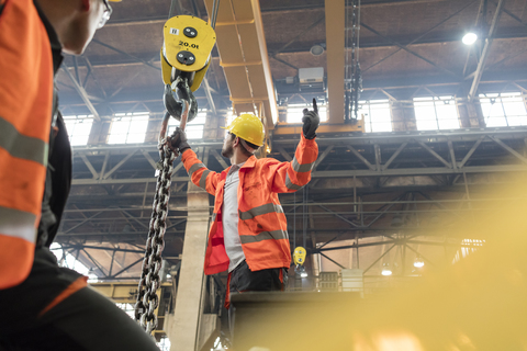 Stahlarbeiter befestigen Kette an Kran in Fabrik, lizenzfreies Stockfoto