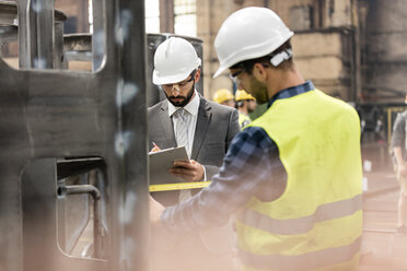 Manager with clipboard and steel worker with tape measure in factory - CAIF09845