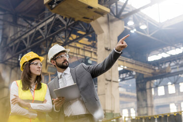 Manager and female steel worker talking looking away in factory - CAIF09846