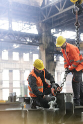 Steel workers fastening crane chain to steel in factory - CAIF09857