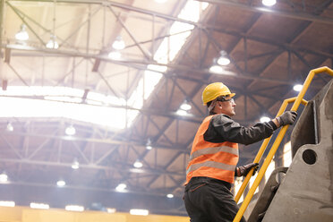 Steel worker climbing ladder in factory - CAIF09860