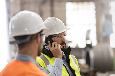 Stahlarbeiter, die in einer Fabrik mit ihrem Handy telefonieren - CAIF09862