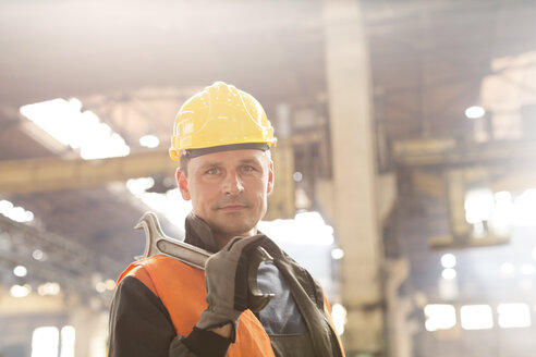 Porträt eines selbstbewussten Stahlarbeiters, der einen großen Schraubenschlüssel in einer Fabrik hält - CAIF09867