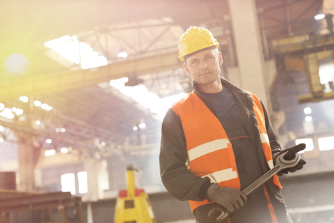 Porträt eines selbstbewussten Stahlarbeiters, der einen großen Schraubenschlüssel in einer Fabrik hält, lizenzfreies Stockfoto