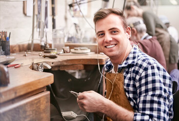 Porträt lächelnder männlicher Juwelier bei der Arbeit, der mit Kopfhörern in einer Werkstatt Musik hört - CAIF09890