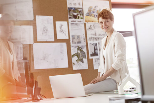 Porträt einer lächelnden Designerin bei der Arbeit am Laptop im Büro - CAIF09908