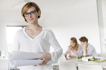 Portrait confident female architect holding blueprints in conference room - CAIF09922