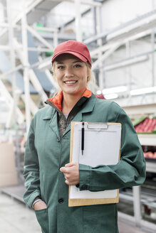 Porträt eines lächelnden Arbeiters mit Klemmbrett in einem Lebensmittelverarbeitungsbetrieb - CAIF09947