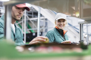 Portrait smiling female worker inspecting apples in food processing plant - CAIF09951