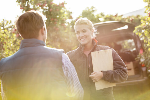 Smiling farmers talking in sunny apple orchard - CAIF09956