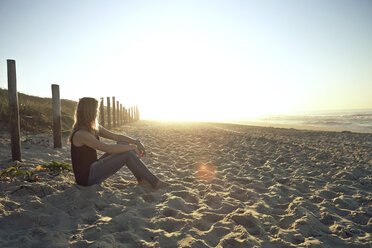 Seitenansicht einer Frau, die bei Sonnenuntergang am Strand sitzt - CAVF04913