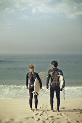 Rückansicht eines Paares, das Surfbretter trägt, während es am Ufer steht - CAVF04924