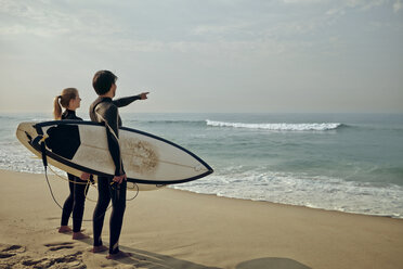 Paar schaut auf das Meer und trägt ein Surfbrett am Strand - CAVF04925