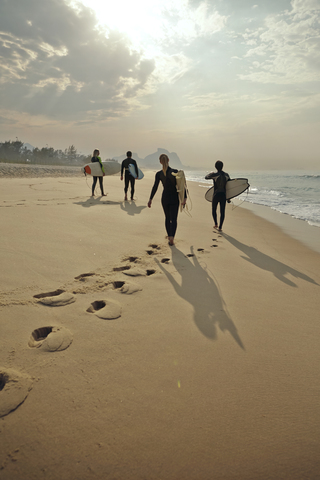 Rückansicht von Freunden, die Surfbretter tragen, während sie auf dem Sand am Strand laufen, lizenzfreies Stockfoto