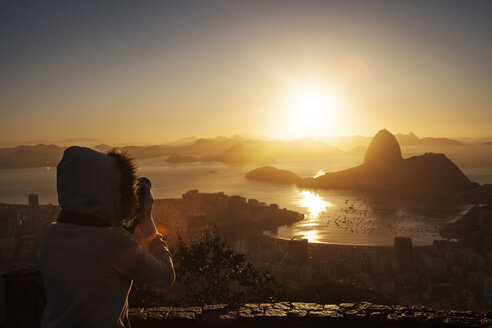 Frau fotografiert den Sugarloaf Mountain, während sie bei Sonnenuntergang am Aussichtspunkt steht - CAVF04938