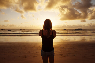 Rear view of woman standing at beach during sunset - CAVF04960