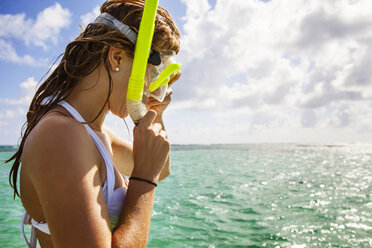 Woman adjusting snorkel while standing in sea against cloudy sky - CAVF04965