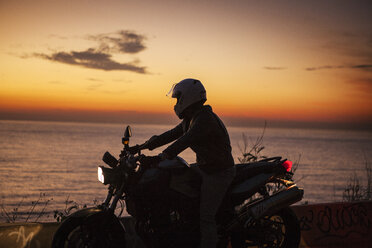Mann fährt Motorrad am Meer gegen den Himmel bei Sonnenuntergang - CAVF04968