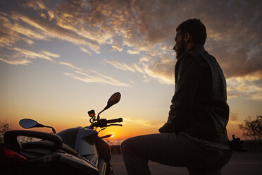 Low angle view of man standing by motorcycle against cloudy sky - CAVF04978