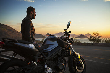 Mann steht mit Motorrad gegen den Himmel bei Sonnenuntergang - CAVF04980