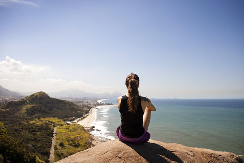 Rear view of woman sitting on rock and looking at view - CAVF04986