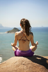 Rear view of woman meditating while sitting on rock - CAVF04988