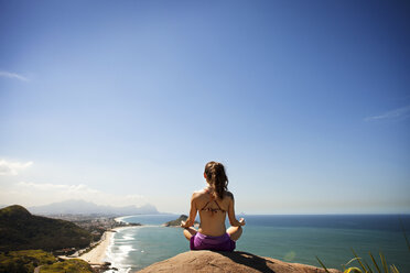 Meditierende Frau, die auf einem Felsen am Meer sitzt - CAVF04989