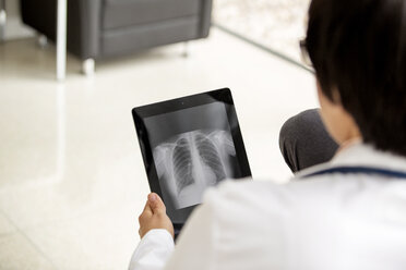 Rückansicht eines Arztes, der einen Röntgenbericht in einem Tablet-Computer betrachtet - CAVF05034