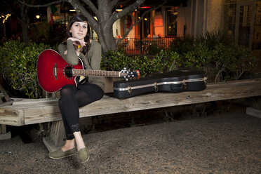 Portrait of woman holding guitar while sitting on bench - CAVF05071