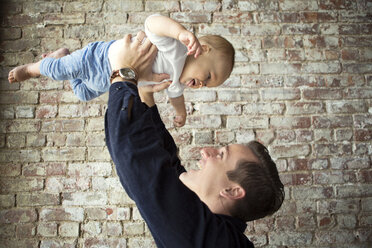 Father playing with son while standing against wall at home - CAVF05098