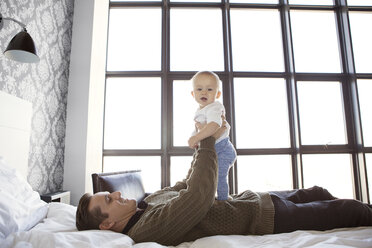 Seitenansicht des Vaters, der mit seinem süßen Sohn spielt, während er zu Hause auf dem Bett liegt - CAVF05115