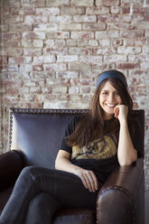 Portrait of cheerful woman sitting on arm chair at home - CAVF05118