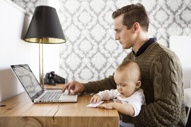 Vater arbeitet am Laptop, während er mit seinem Sohn am Tisch sitzt - CAVF05121