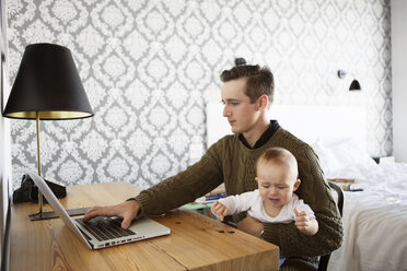 Man using laptop while sitting with son at table in home - CAVF05122