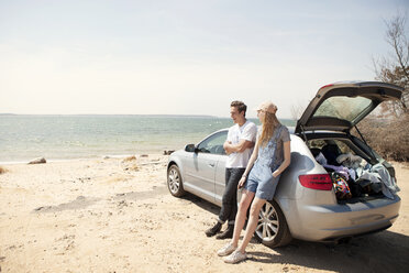 Friends leaning on car while standing at beach against sky - CAVF05149