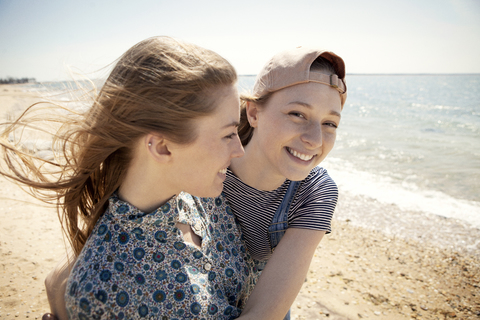 Porträt einer glücklichen Frau, die ihren Freund umarmt, während sie am Strand steht, lizenzfreies Stockfoto