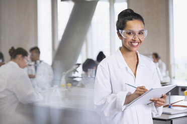 Porträt einer lächelnden Studentin, die in einem wissenschaftlichen Laboratorium Notizen macht - CAIF10010