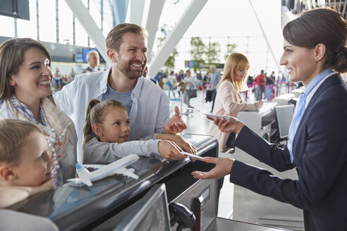 Kundendienstmitarbeiter, der einer Familie beim Einchecken mit Tickets am Flughafen hilft - CAIF10015