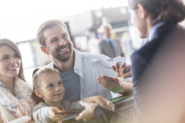 Kundendienstmitarbeiter, der einer Familie am Check-in-Schalter des Flughafens mit den Tickets hilft - CAIF10016