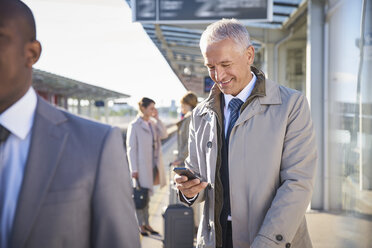 Geschäftsmann, der mit seinem Handy vor dem Flughafen SMS schreibt - CAIF10036