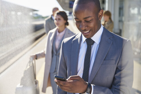 Geschäftsmann, der auf dem Bahnsteig eine SMS mit seinem Mobiltelefon schreibt - CAIF10042