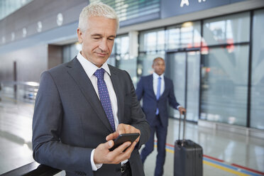 Geschäftsmann, der in einer Flughafenhalle mit seinem Mobiltelefon SMS schreibt - CAIF10045