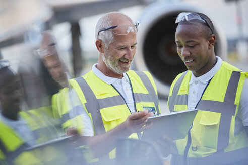 Mitarbeiter des Bodenpersonals der Flugsicherung unterhalten sich auf dem Rollfeld eines Flughafens mit einem digitalen Tablet - CAIF10051