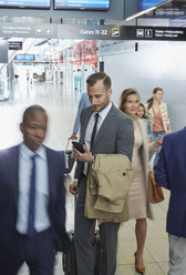 Geschäftsmann benutzt Mobiltelefon in einer Flughafenhalle - CAIF10062