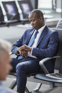 Geschäftsmann, der die Zeit auf seiner Armbanduhr überprüft, während er im Abflugbereich des Flughafens wartet - CAIF10066