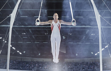 Männlicher Turner balanciert mit ausgestreckten Armen auf Gymnastikringen in einer Arena - CAIF10068