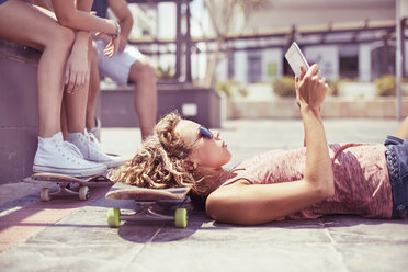Junge Frau mit digitalem Tablet auf dem Skateboard liegend - CAIF10128