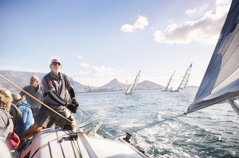 Mann beim Einstellen der Takelage eines Segelboots auf dem sonnigen Meer, lizenzfreies Stockfoto